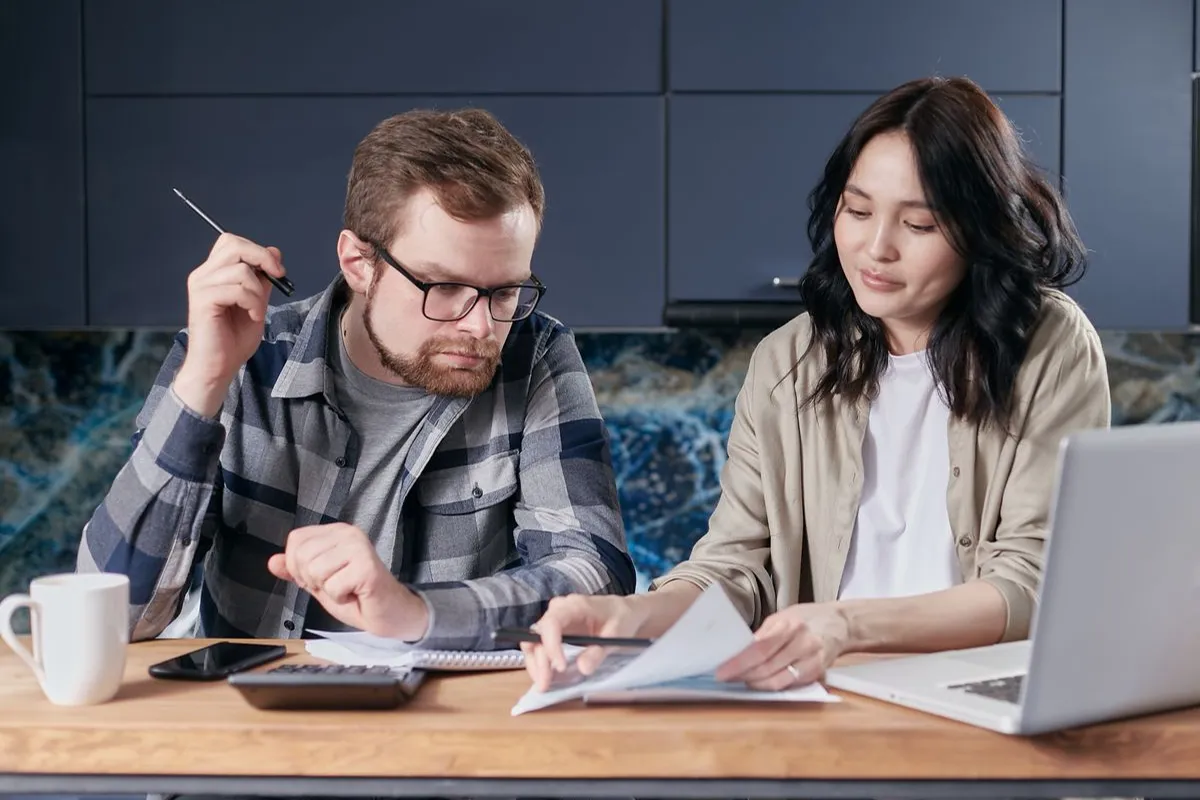 A couple reviewing paperwork together at a table with a calculator and laptop.